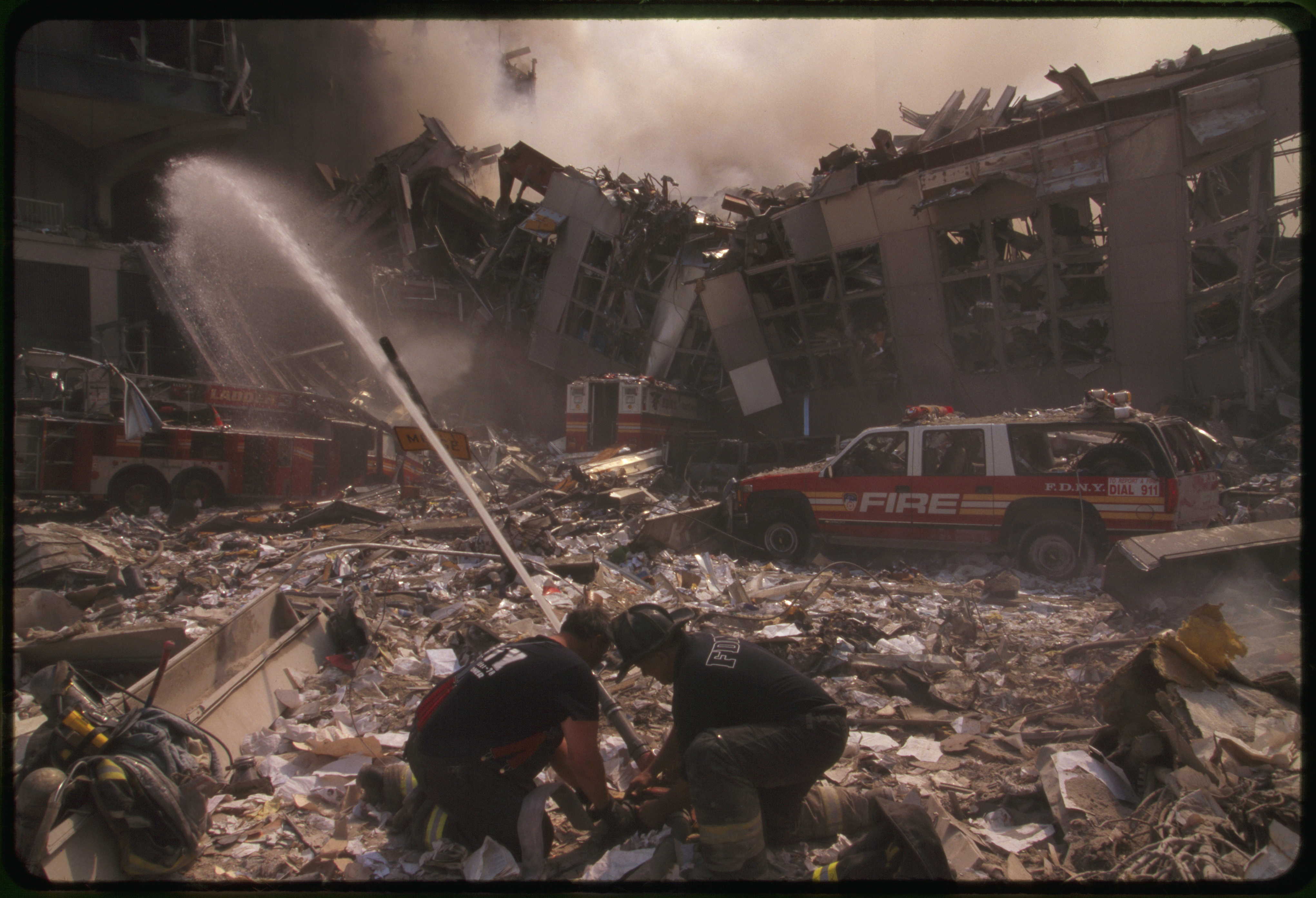 Two New York City fire fighters spraying water on smoldering ruins following September 11th terrorist attack on World Trade Center, New York City