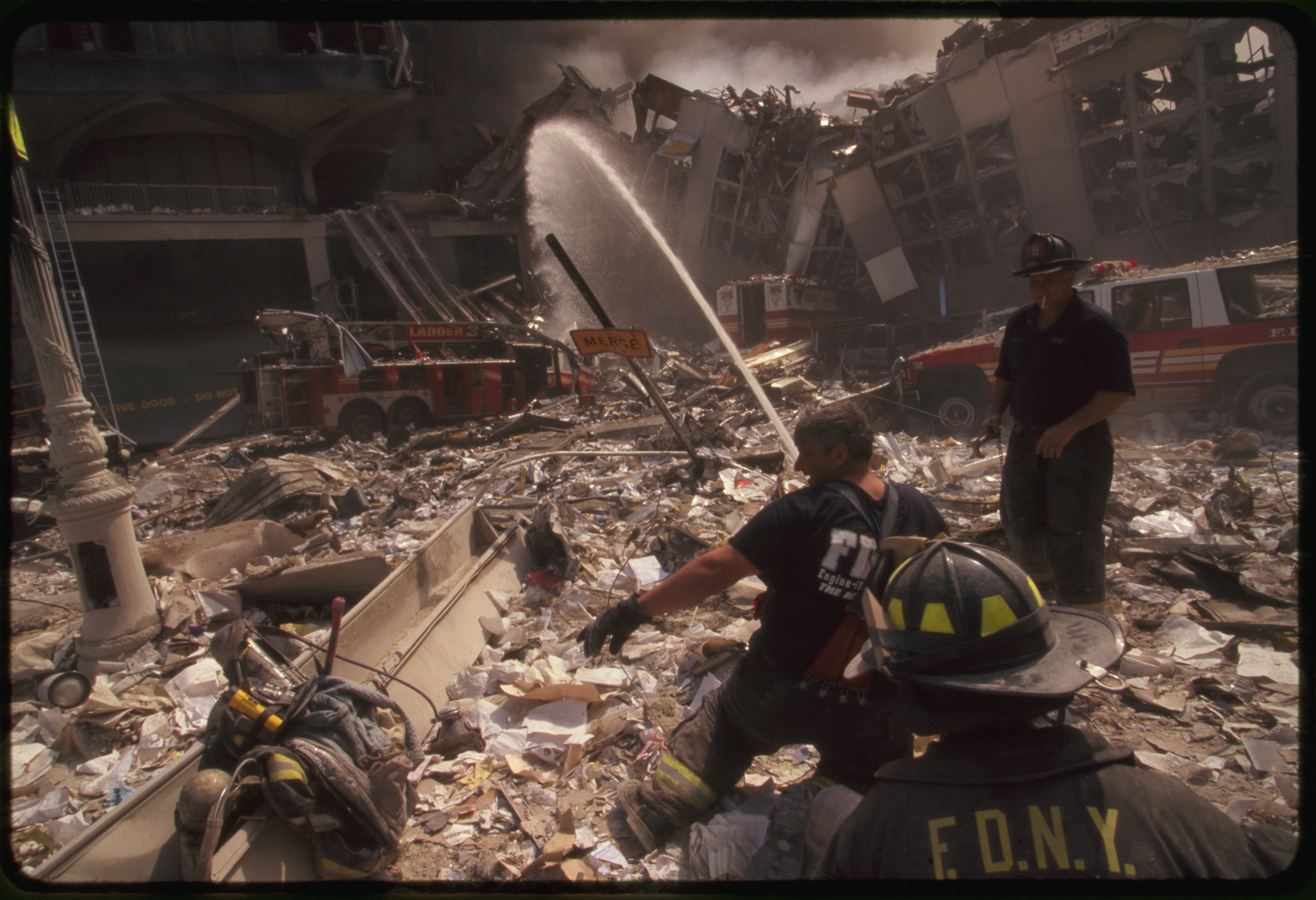 Three New York City fire fighters spraying water on smoldering ruins following September 11th terrorist attack on World Trade Center, New York City