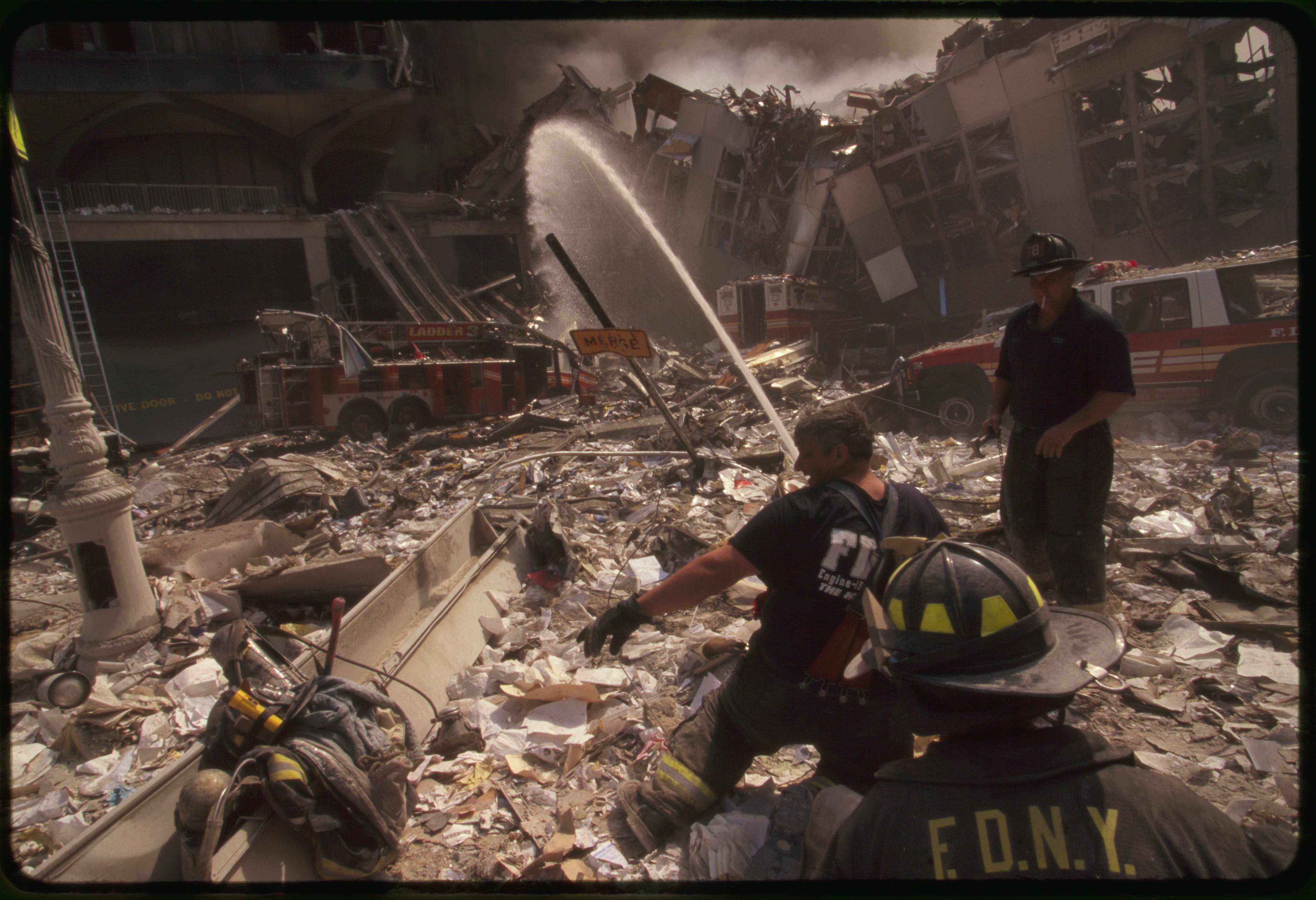 Three New York City fire fighters spraying water on smoldering ruins following September 11th terrorist attack on World Trade Center, New York City
