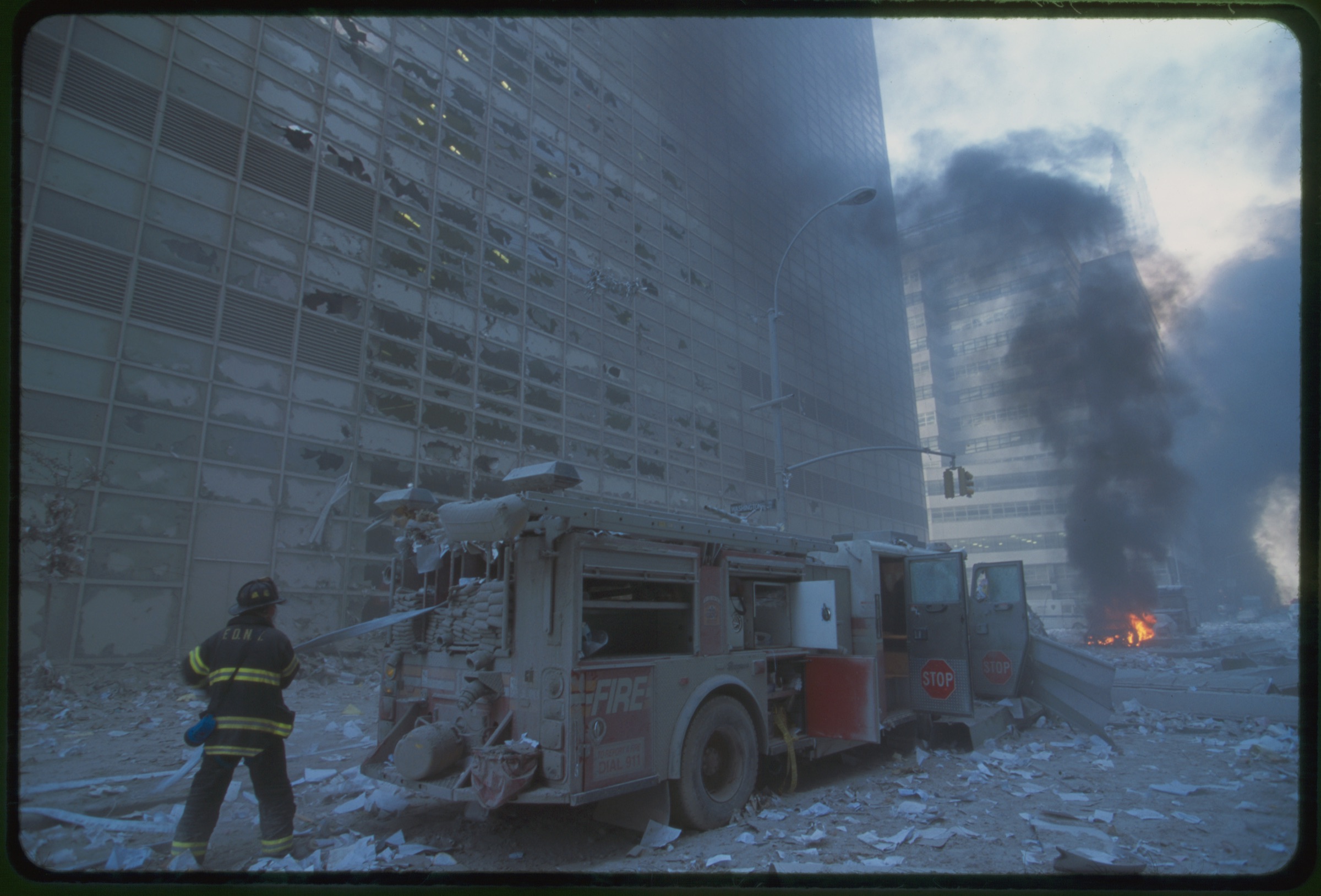 New York City fire fighter pulling water hose from fire truck amid debris and burning buildings following September 11th terrorist attack on World Trade Center, New York City